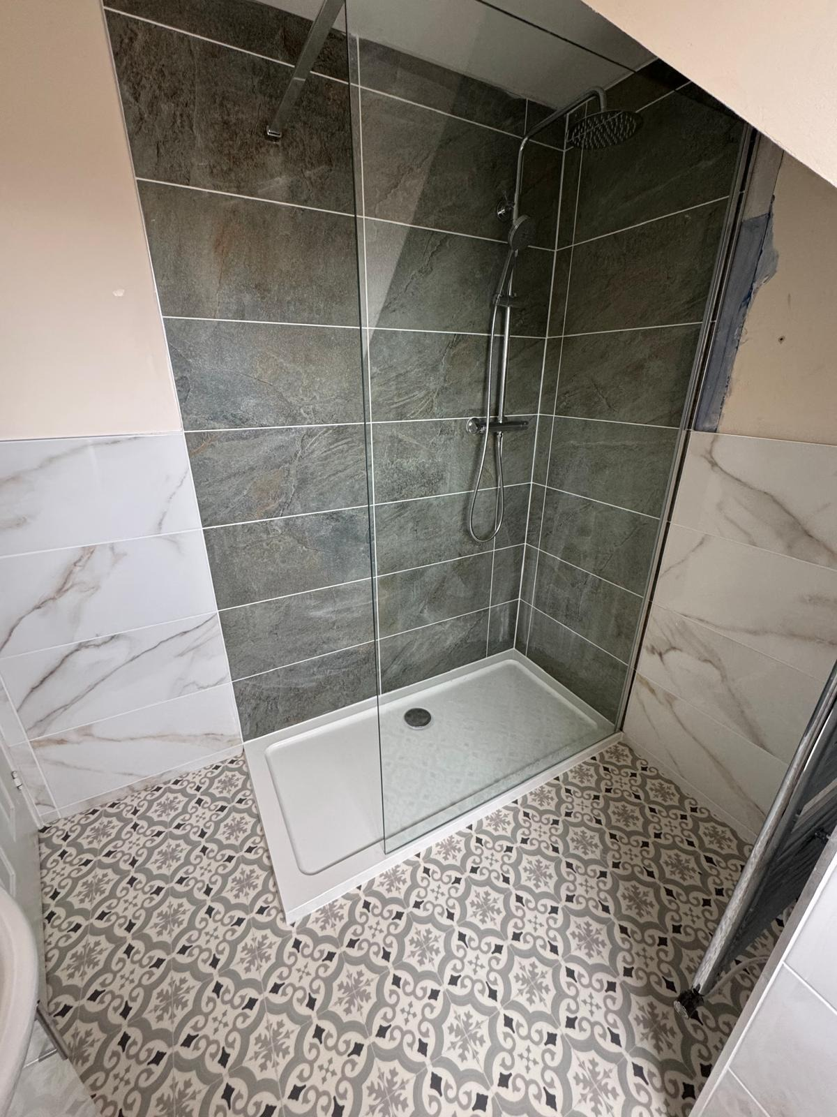 Walk-in shower with slate-effect wall tiling, rainfall head and patterned floor tiles in a completed bathroom installation