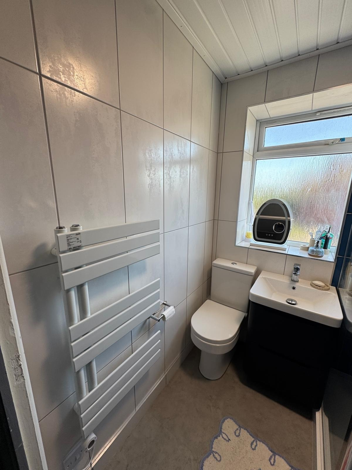 Tiled bathroom with heated towel rail, WC and basin vanity beside a frosted window